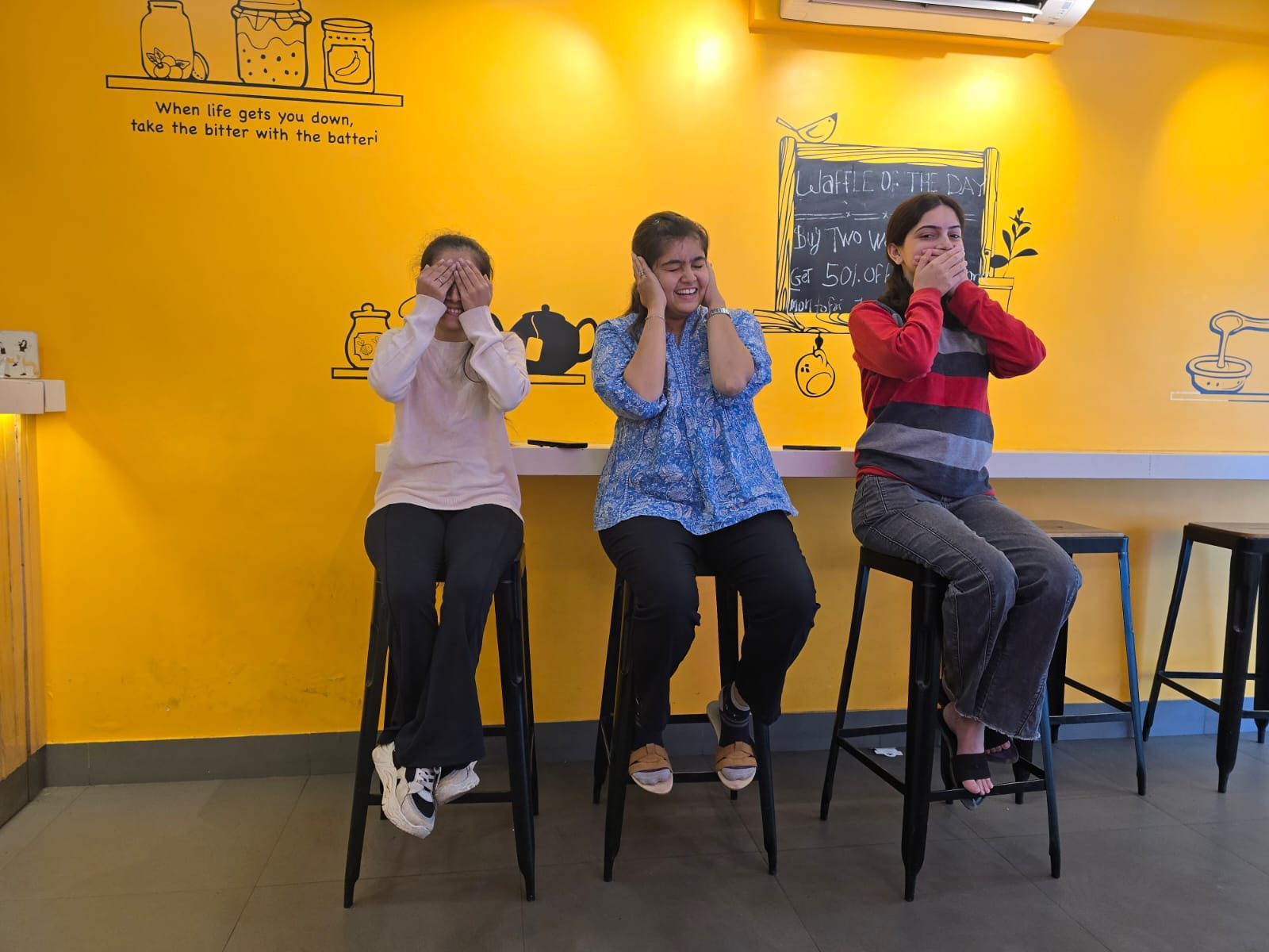 Three team members striking a fun see-no-evil, hear-no-evil, speak-no-evil pose at a café during a team outing